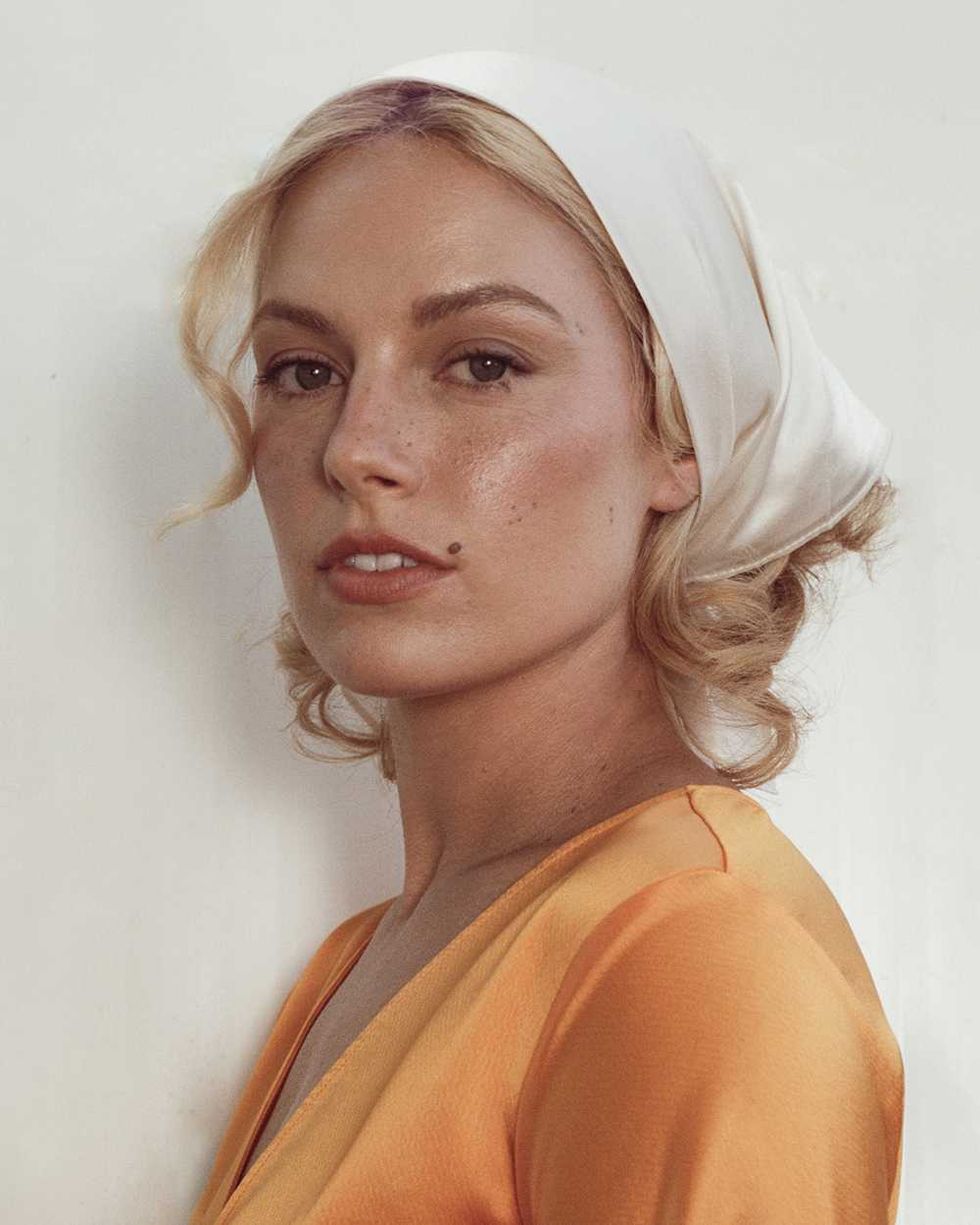 Ashe in an orange top and white headscarf, looking sideways.