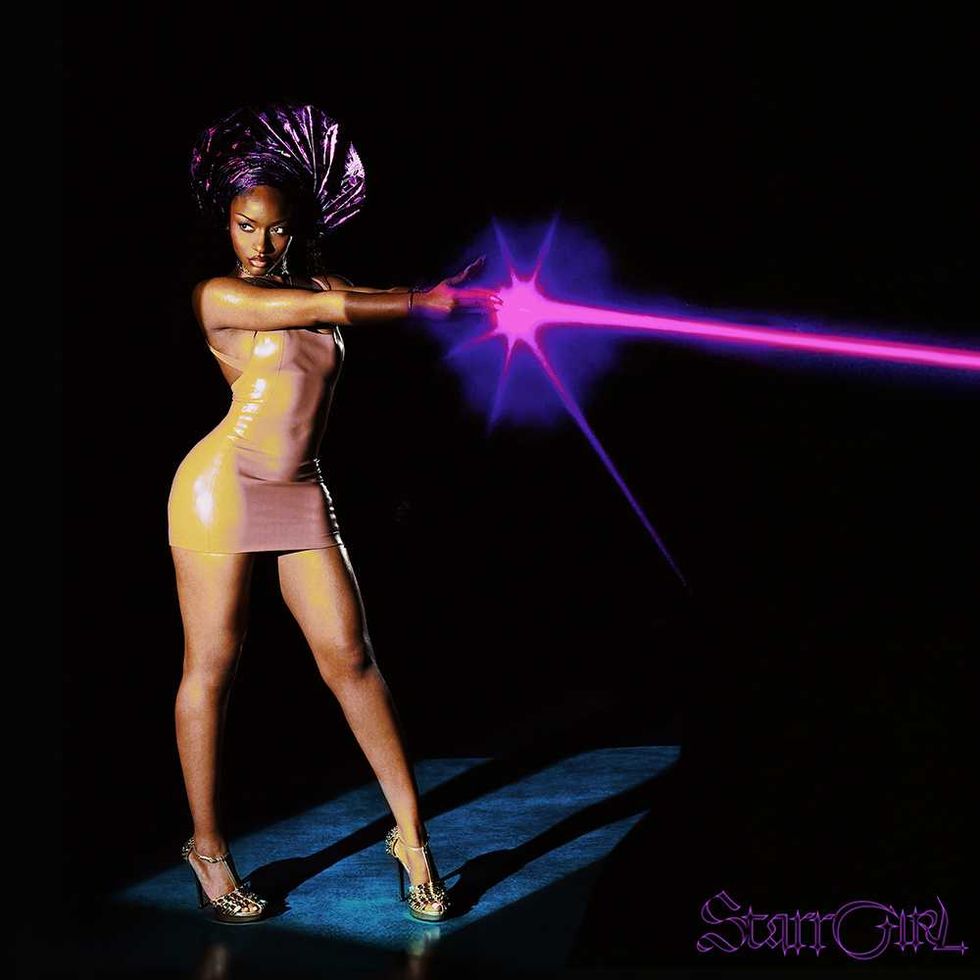 Ayra Starr in a latex dress shoots a pink energy beam from her hand with a dramatic pose.