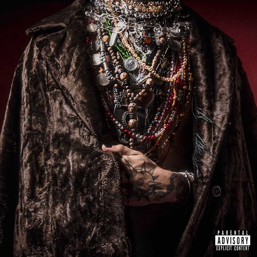 Person in fur coat with layered necklaces, tattoos on hand, "Parental Advisory" label.