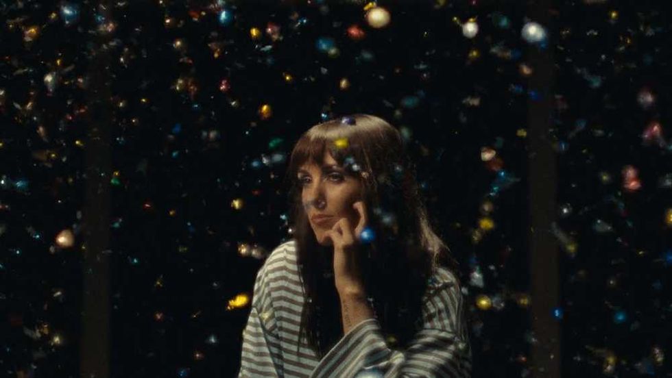 Sasha Alex Sloan in striped shirt gazes through falling confetti, deep in thought.