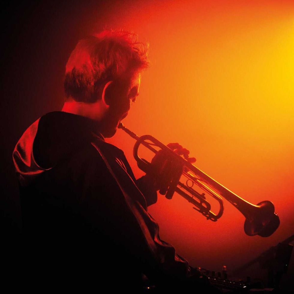 Silhouette of Takuya Nakamura playing trumpet against an orange-red gradient background.