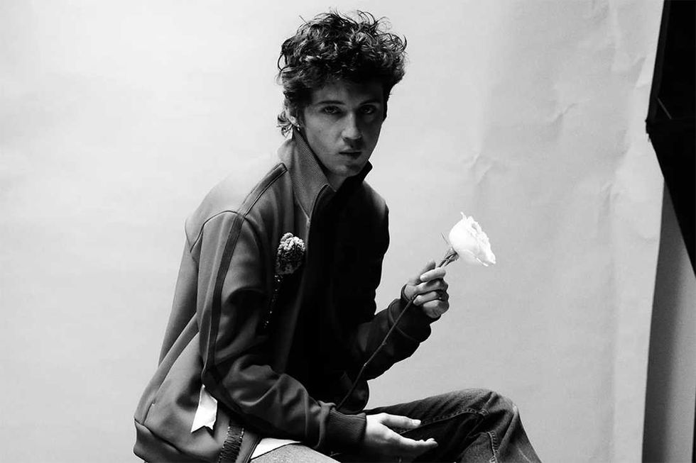 Troye Sivan seated holding a rose, black and white photo.
