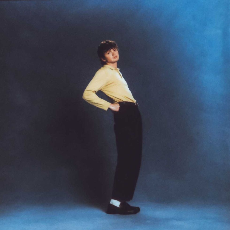 Will Linley in yellow shirt and black pants poses against a blue background.